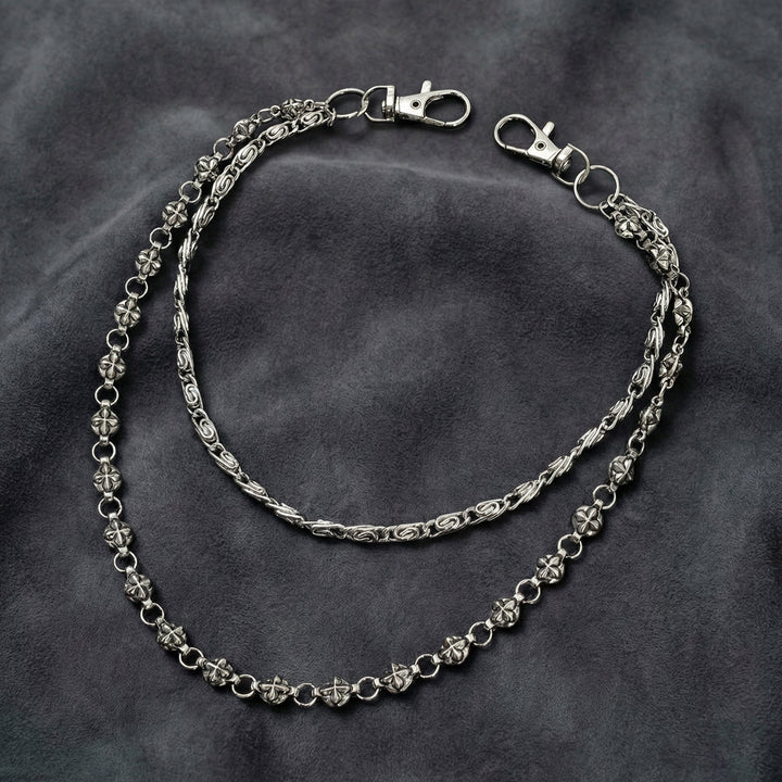 Handcrafted Manor Guardian dual-strand gothic wallet chain with ornate cross links and floral clasps draped on dark charcoal suede.