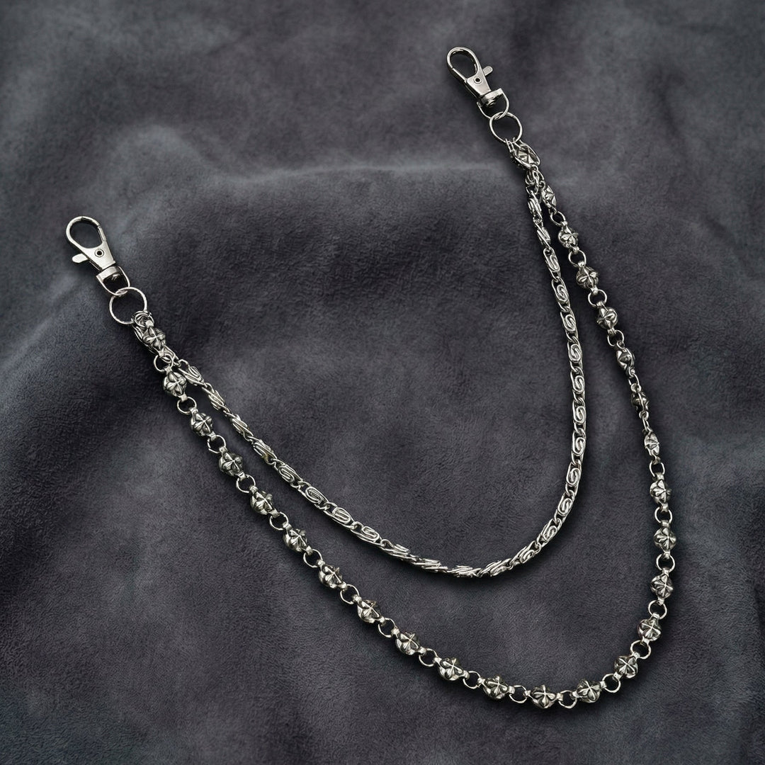 Handcrafted Manor Guardian dual-strand gothic wallet chain with ornate cross links and floral clasps draped on dark charcoal suede.